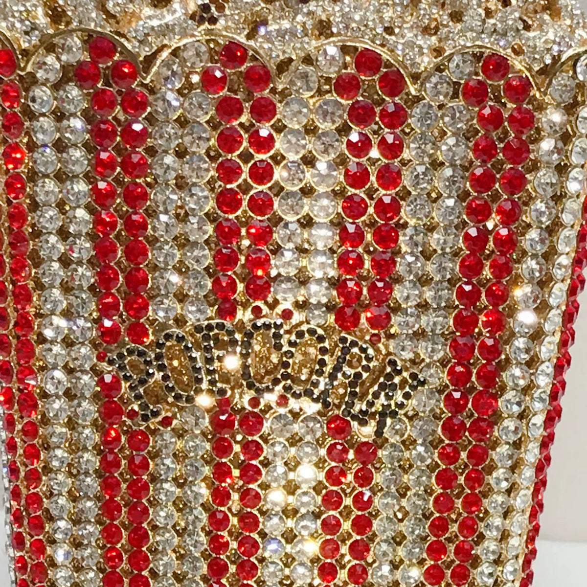 A close-up of a gold-tone popcorn-shaped embellished container or basket covered in red and clear rhinestones, with a decorative 'POP CORN' detail on the front.
