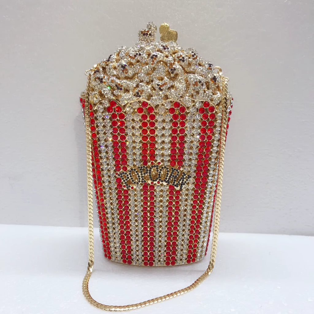 A popcorn-shaped evening bag covered in gold and red rhinestones, with a gold chain strap and a small gold heart on top, photographed against a plain light background.